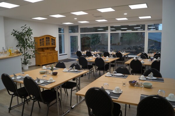 A conference room with multiple tables and chairs, large windows, and a wooden cabinet with a plant.