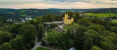 A castle surrounded by lush greenery, with a winding road leading to the entrance.