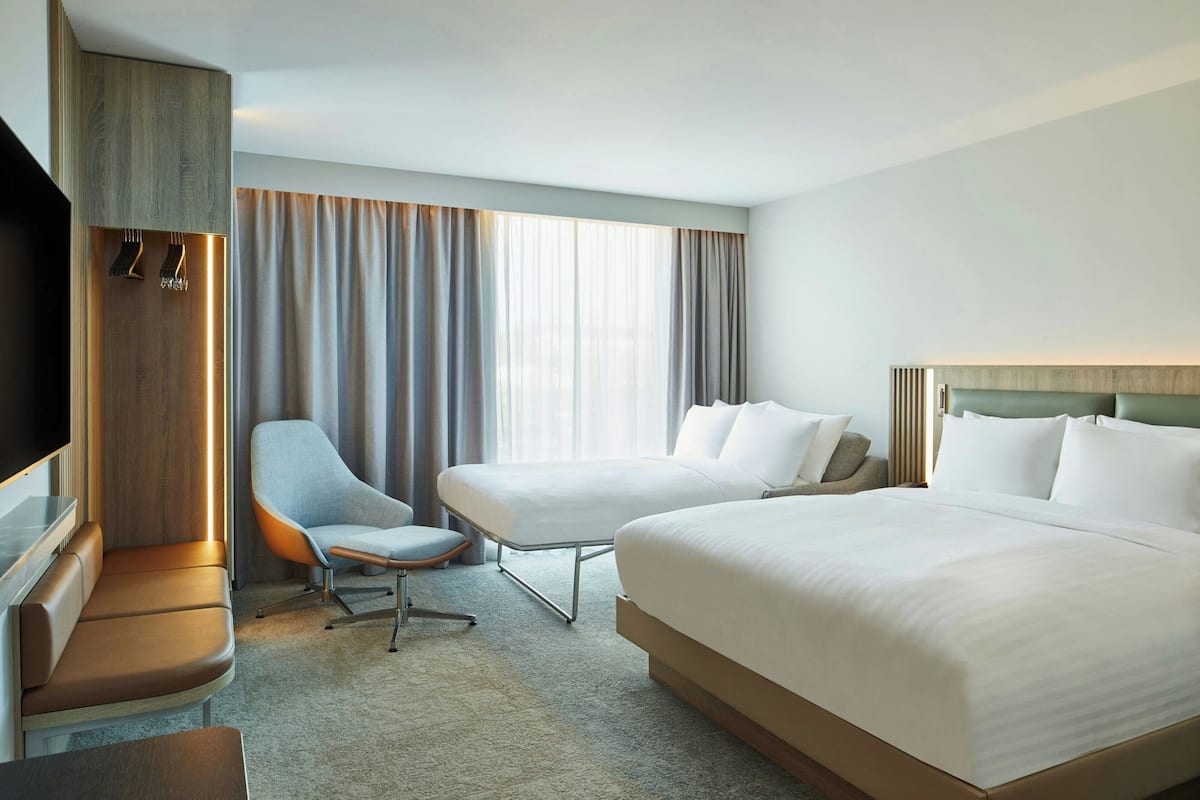 Quarto de hotel com uma cama grande, um sofá, uma cadeira, uma televisão e uma janela com cortinas.