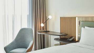 Una habitación de hotel con una cama, un escritorio con teléfono, una silla y una lámpara.