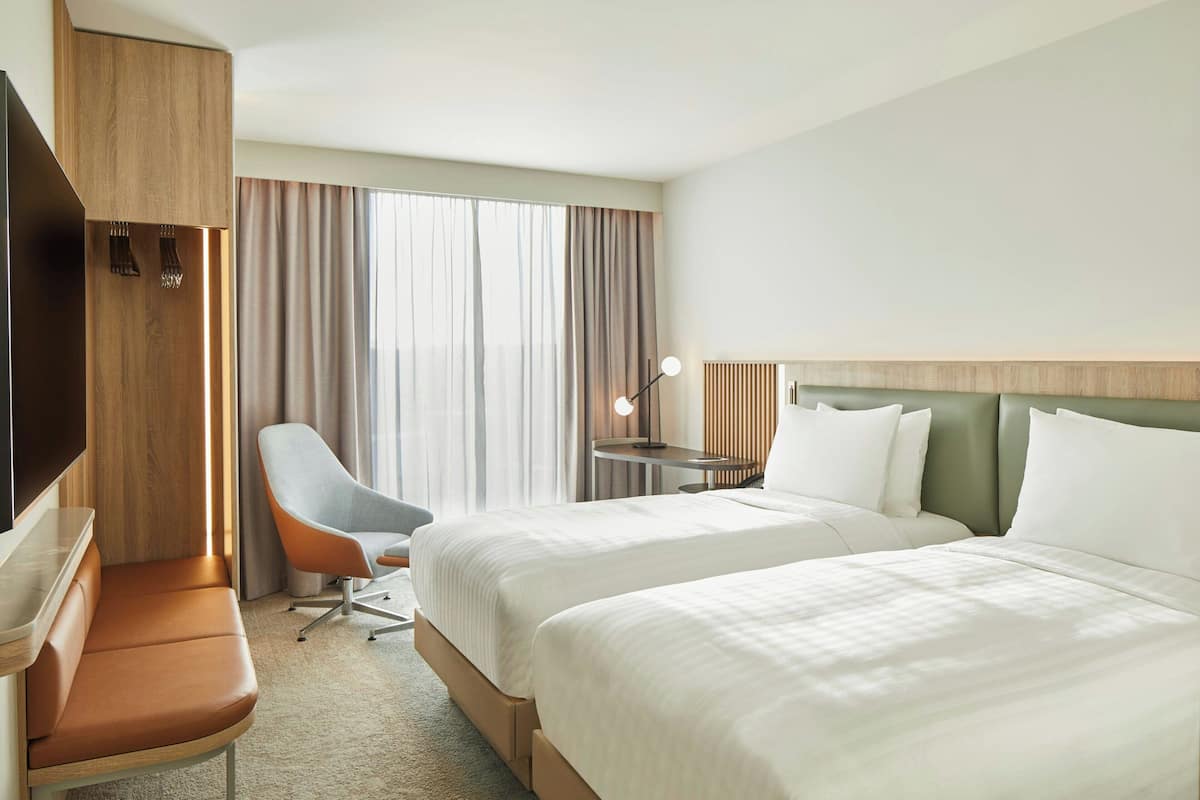Quarto de hotel com duas camas, área de estar, escrivaninha, televisão e janela com cortinas.