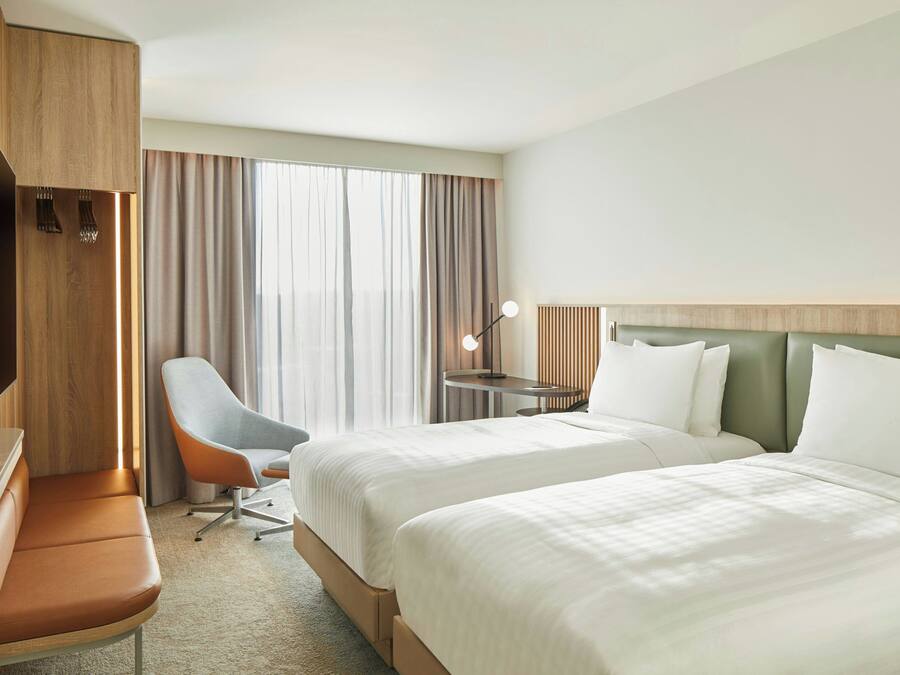 A hotel room with two beds, a seating area, a desk, a TV, and a window with curtains.