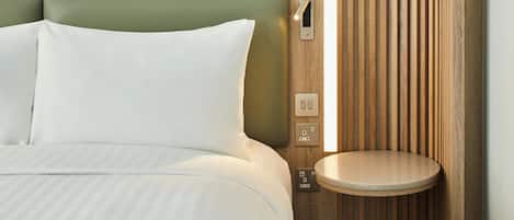 A hotel room with a bed, a bedside table, and a wall-mounted light fixture.