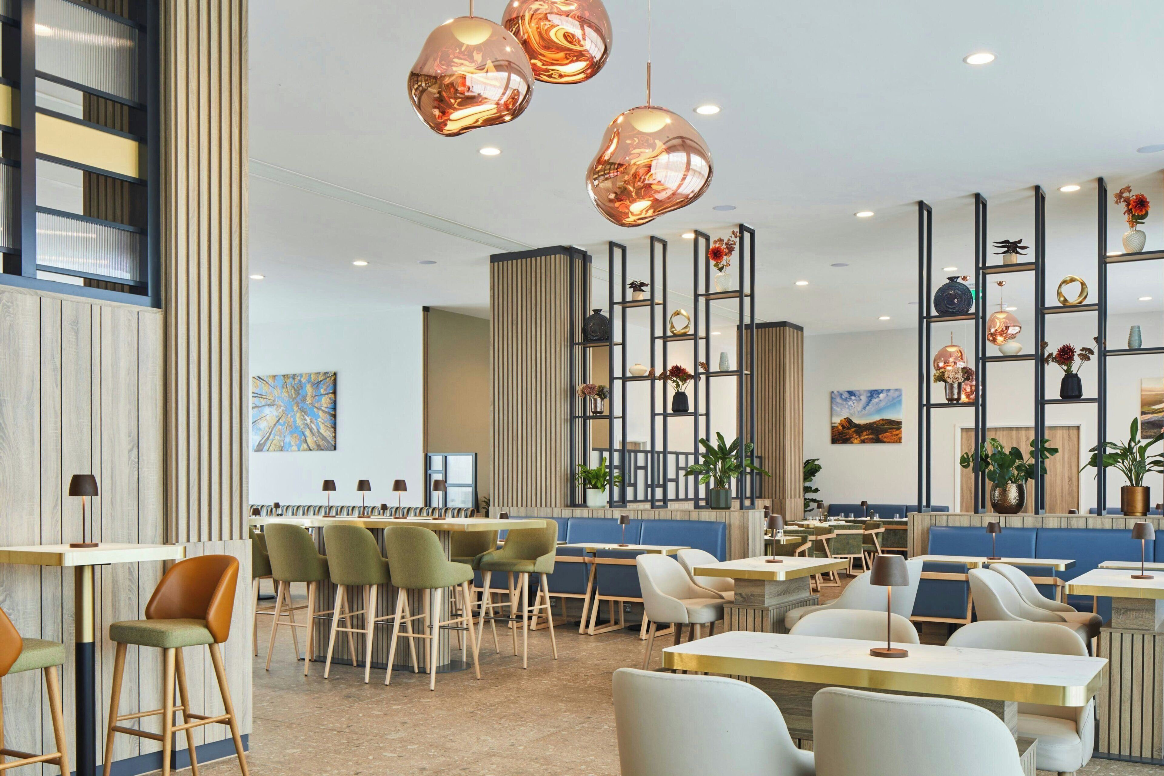 A modern restaurant interior with high ceilings, pendant lighting, and a variety of seating options including booths and tables.