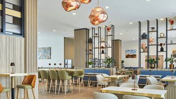 A modern restaurant interior with high ceilings, pendant lighting, and a variety of seating options including booths and tables.