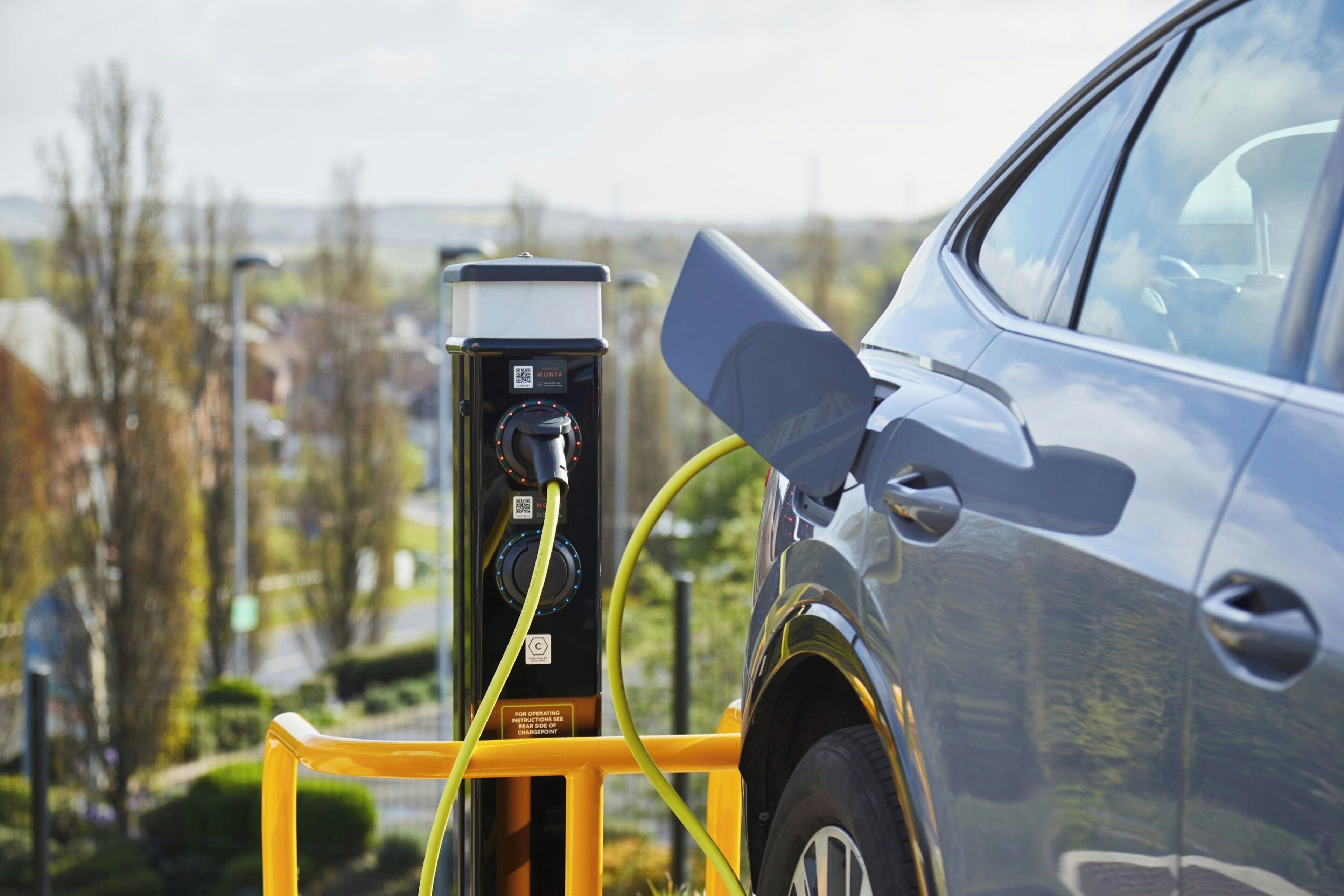 A car charging at a public station with a yellow safety barrier.