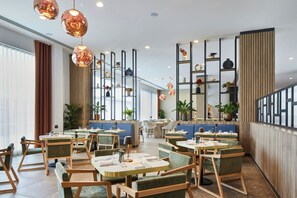 Interior de restaurant modern amb taules rodones, cadires amb coixí, il·luminació penjant i diversos objectes decoratius a les prestatgeries.