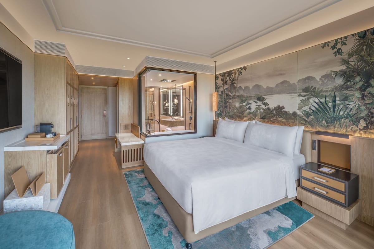 A modern hotel room with a large bed, a desk, and a bathroom visible through an open door.
