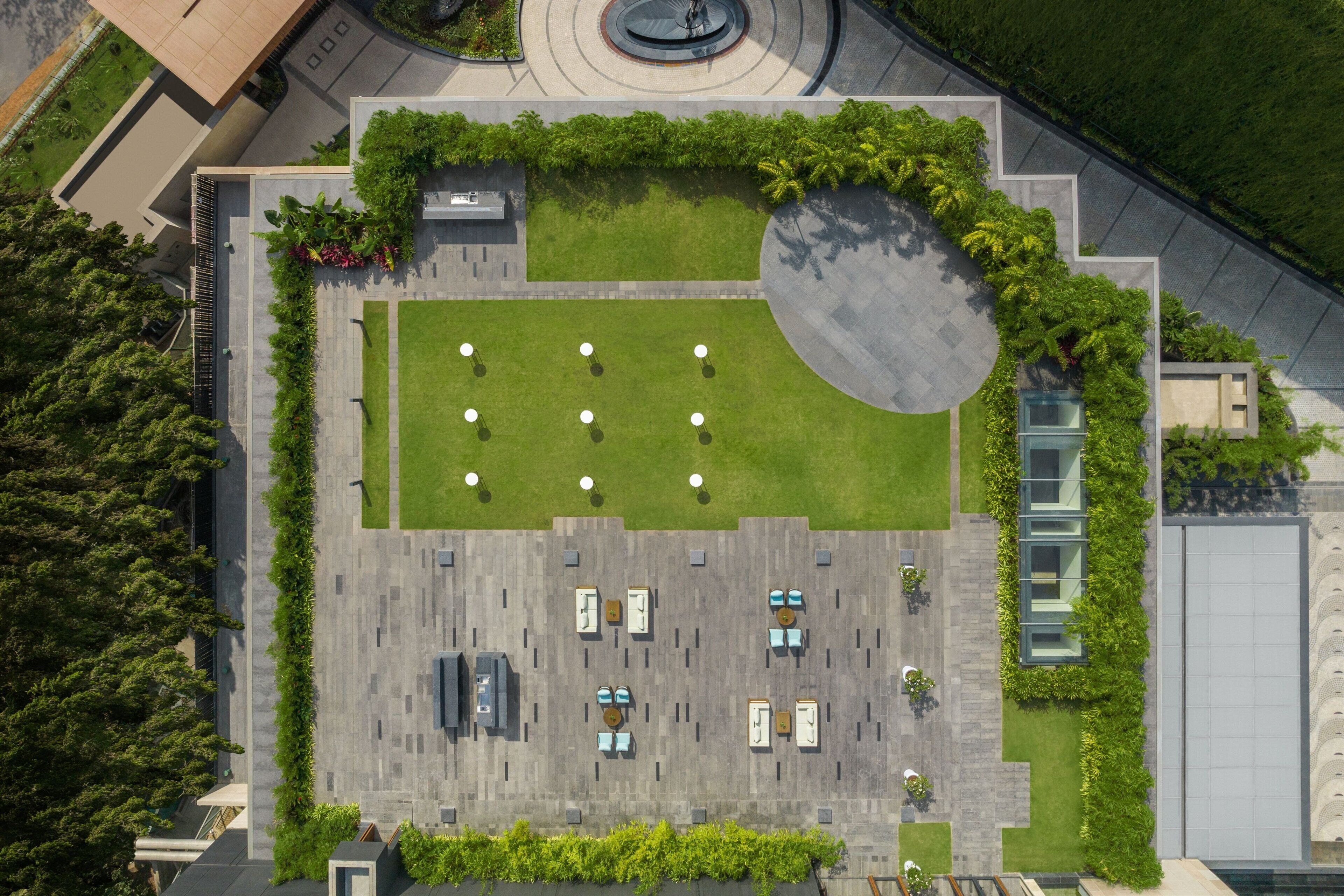 An aerial view of a hotel with a central courtyard, surrounded by greenery and a circular water feature.