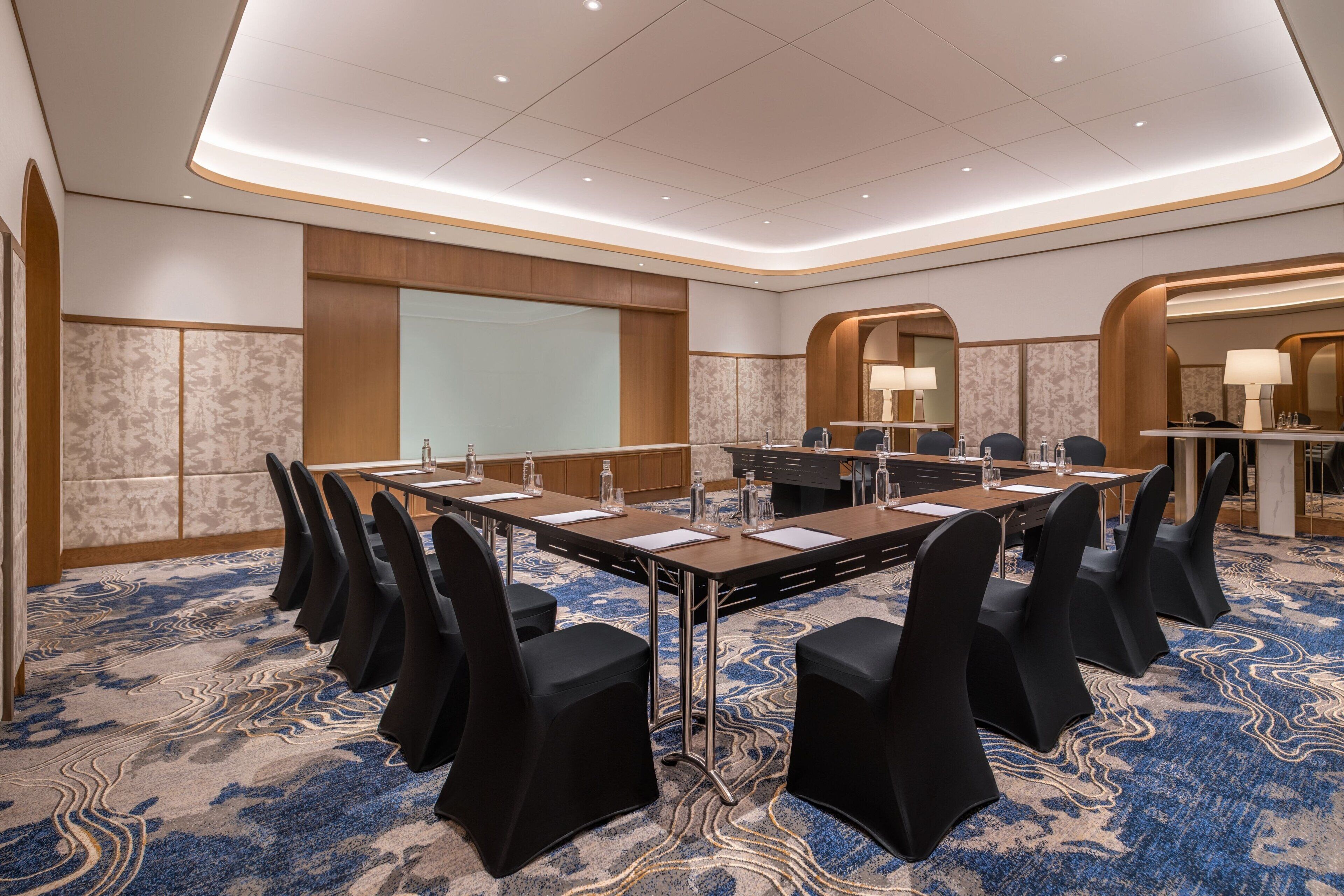 A conference room with a long table, black chairs, and a patterned carpet.