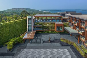 Un hotel moderno con piscina en la azotea, abundante vegetación y vistas panorámicas al océano.