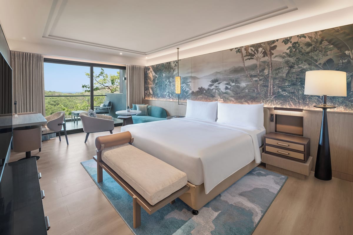 A modern hotel room with a large bed, a desk, a chair, a sofa, and a view of the outdoors.