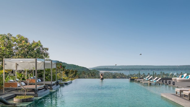 A pool area with lounge chairs and a canopy, surrounded by greenery and hills in the background.