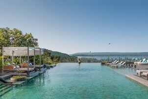 Un área de piscina con sillones de descanso y una pérgola, rodeada de follaje y colinas al fondo.