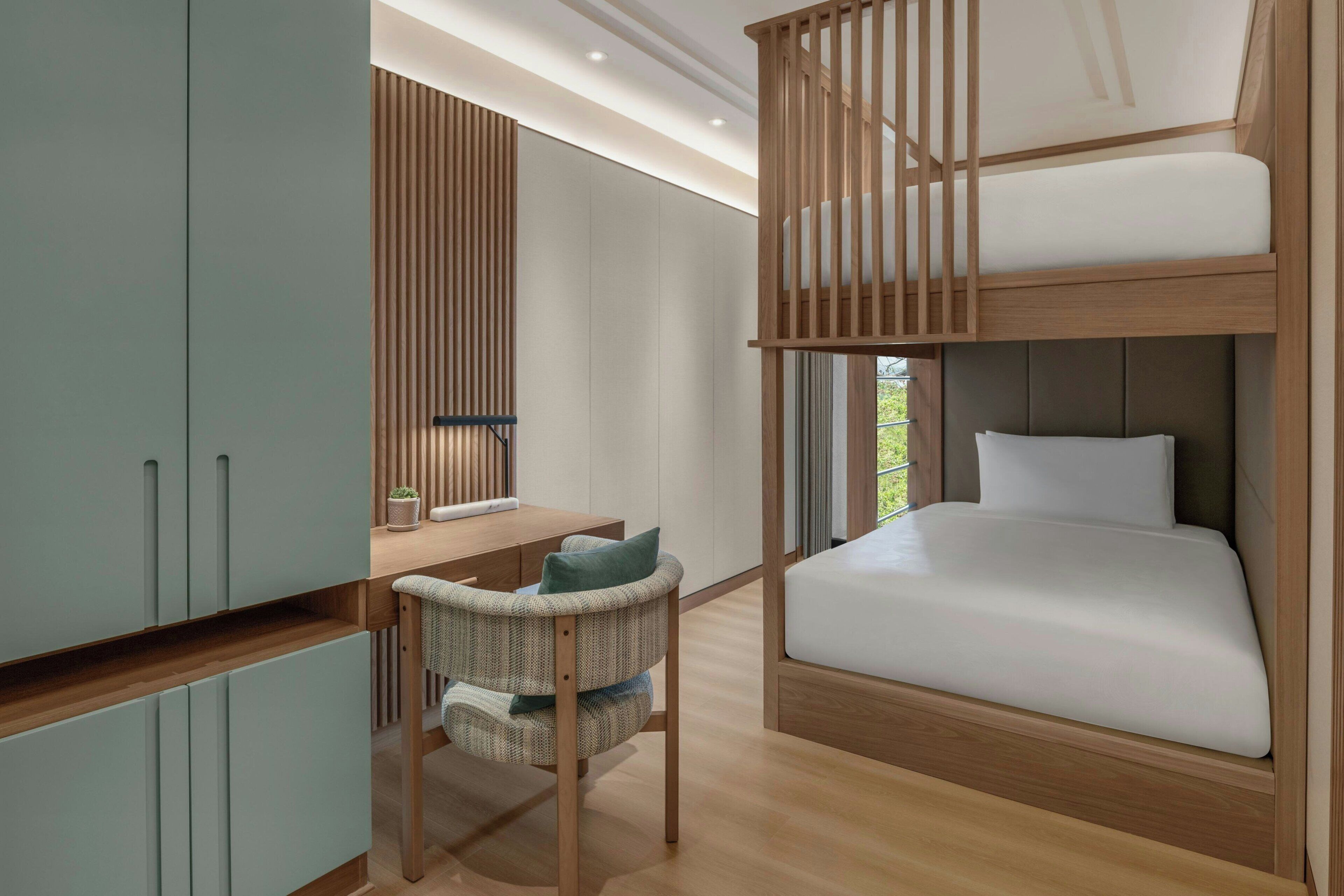 A modern bedroom with a bunk bed, a desk with a chair, and built-in wardrobes.