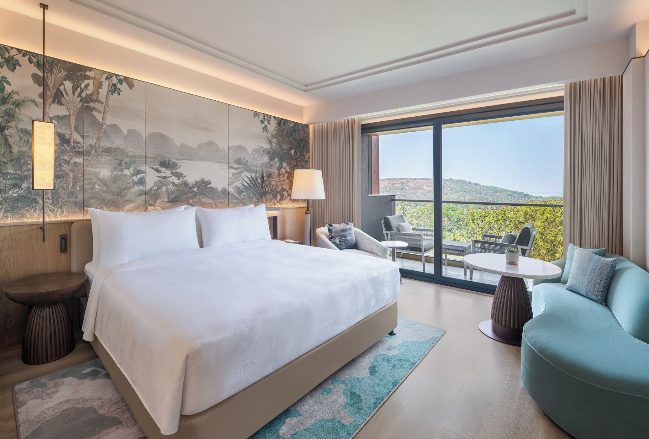 A hotel room with a large bed, a sofa, a dining table, and a view of the outdoors.