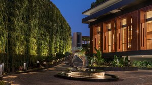 A modern building with a wooden facade and large windows, surrounded by a landscaped garden with a central water feature.