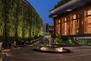 Un edificio moderno con fachada de madera y ventanas grandes, rodeado de un jardín ajardinado con una fuente central.