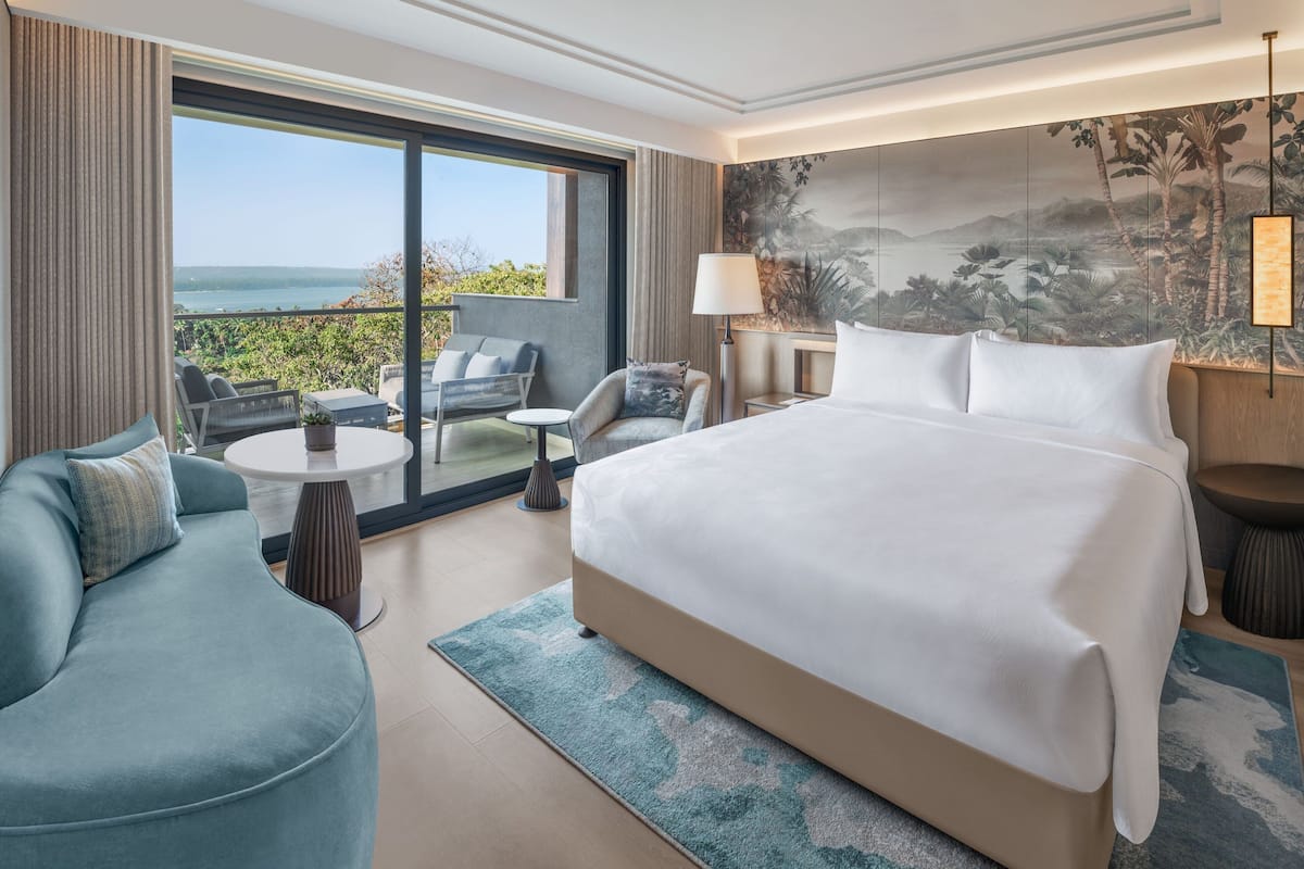 A hotel room with a large bed, a sofa, a small table, and a view of the outdoors.