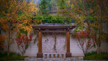 A gazebo with a stone base and a metal railing, surrounded by trees with autumn foliage.