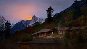 A mountain lodge with a stone facade, large windows, and a well-lit interior. - Rissai Valley, a Ritz-Carlton Reserve (Ngawa Autonomous Prefecture)
