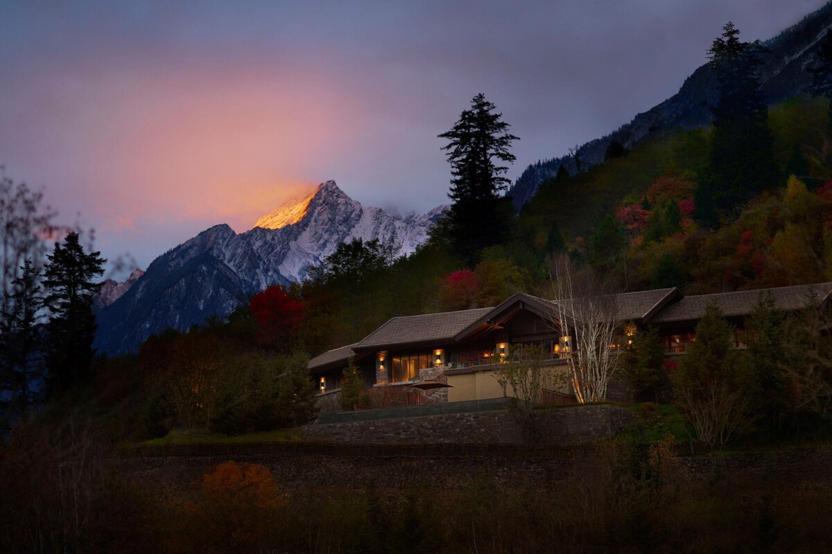 Un albergue de montaña con fachada de piedra, ventanas amplias y un interior luminoso.