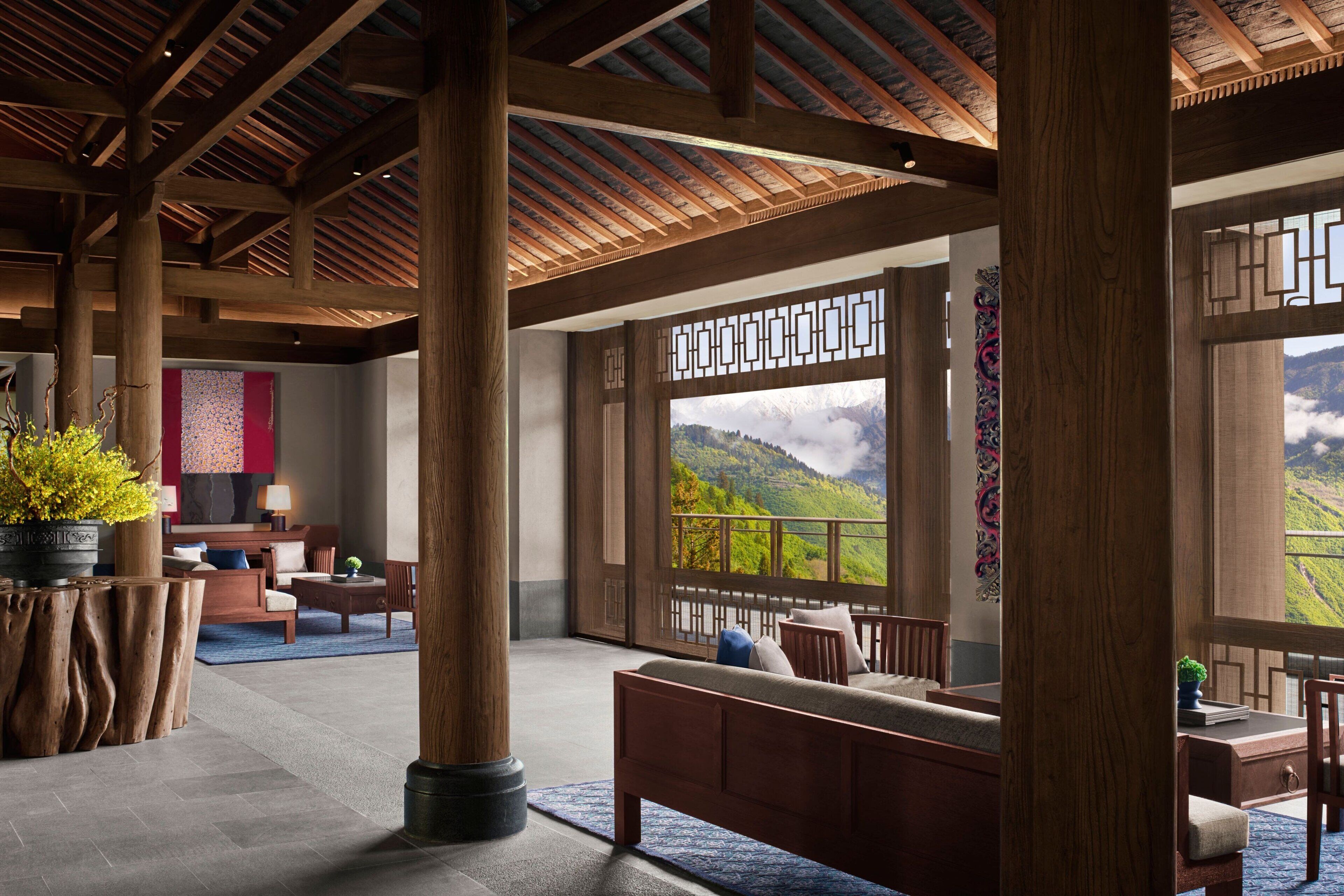 Eine großzügige Lobby mit Holzboden, großen Fenstern mit Blick auf die Berge, einer Sitzecke mit Sofa und Sesseln und einer Zimmerpflanze.