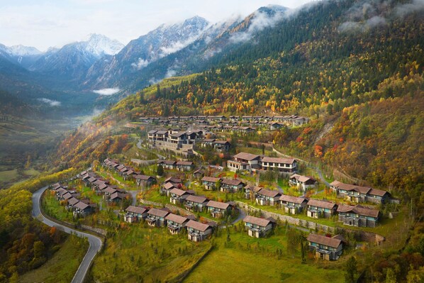A residential area with houses arranged in a semi-circular pattern around a central road, surrounded by mountainous terrain and autumn foliage. - Rissai Valley, a Ritz-Carlton Reserve (Ngawa Autonomous Prefecture)