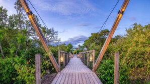 A wooden pedestrian bridge with lantern-style lighting, surrounded by greenery.
