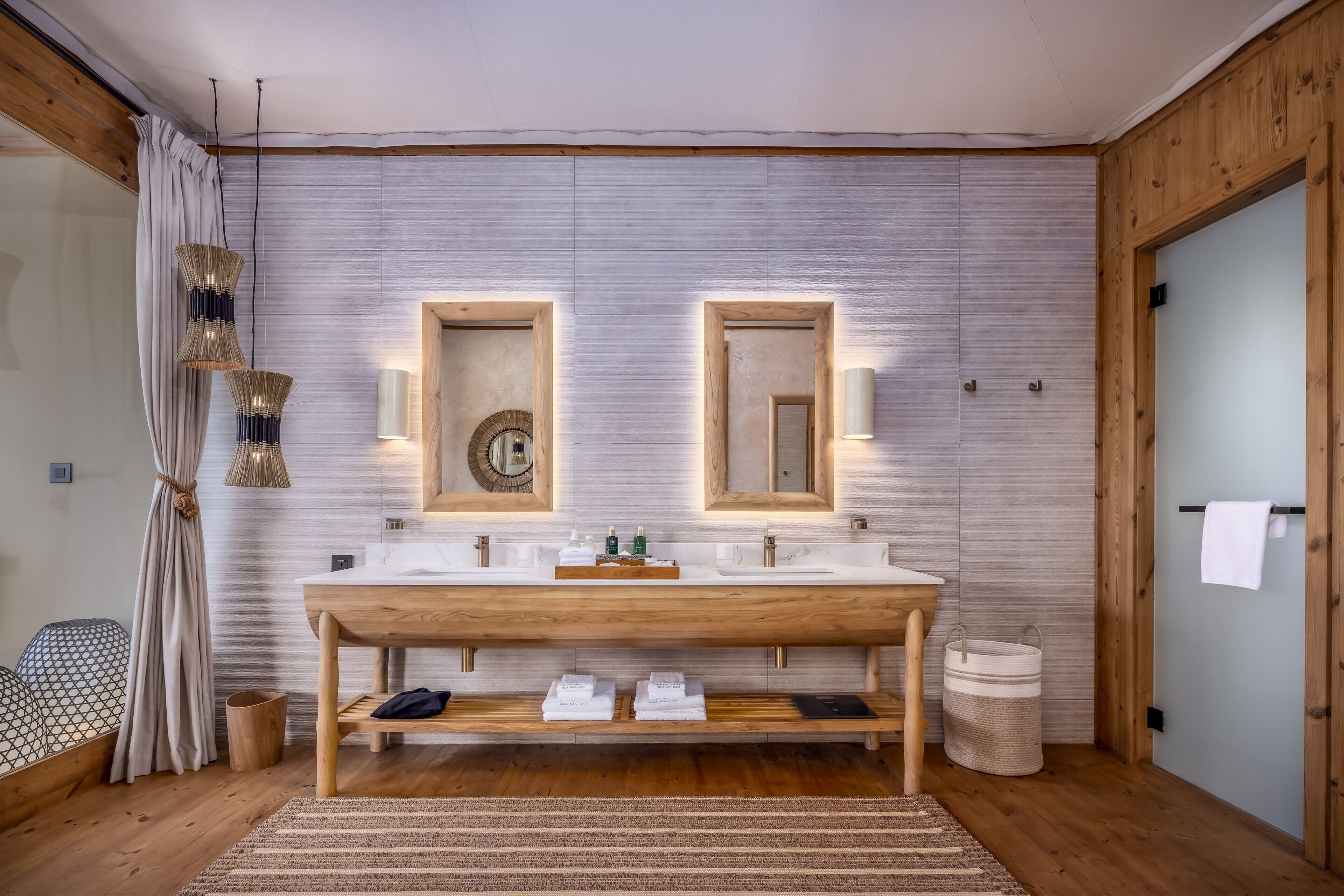 Un baño moderno con tocador de madera, dos espejos y un espejo grande sobre el lavamanos.