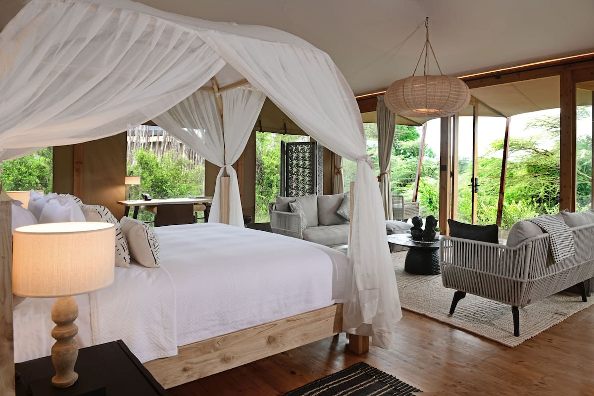 Un dormitorio con cama con dosel, un sofá y una zona de comedor con vistas a zonas verdes.