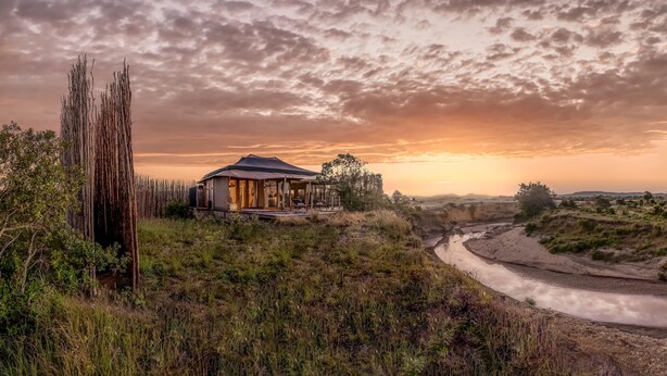A rustic house with a porch, surrounded by natural landscape and a river.