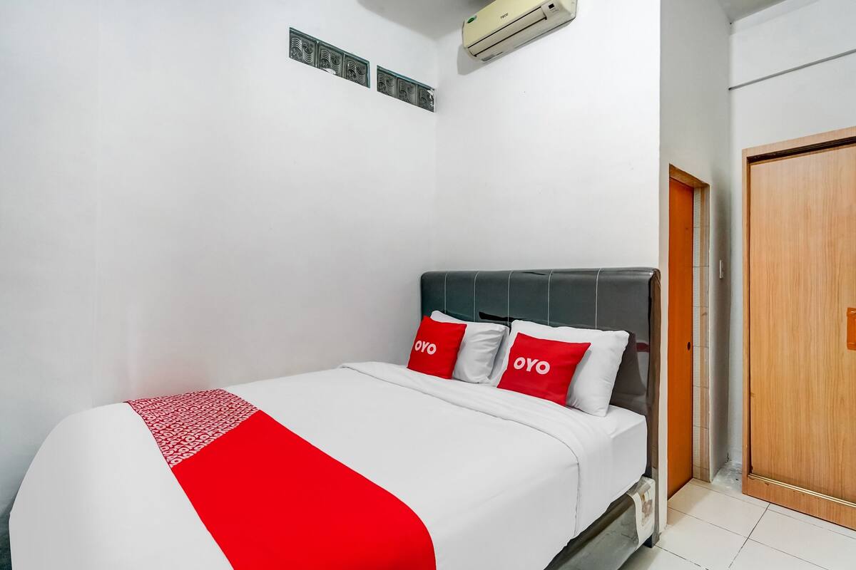 A hotel room with a bed, a wooden door, and an air conditioning unit.