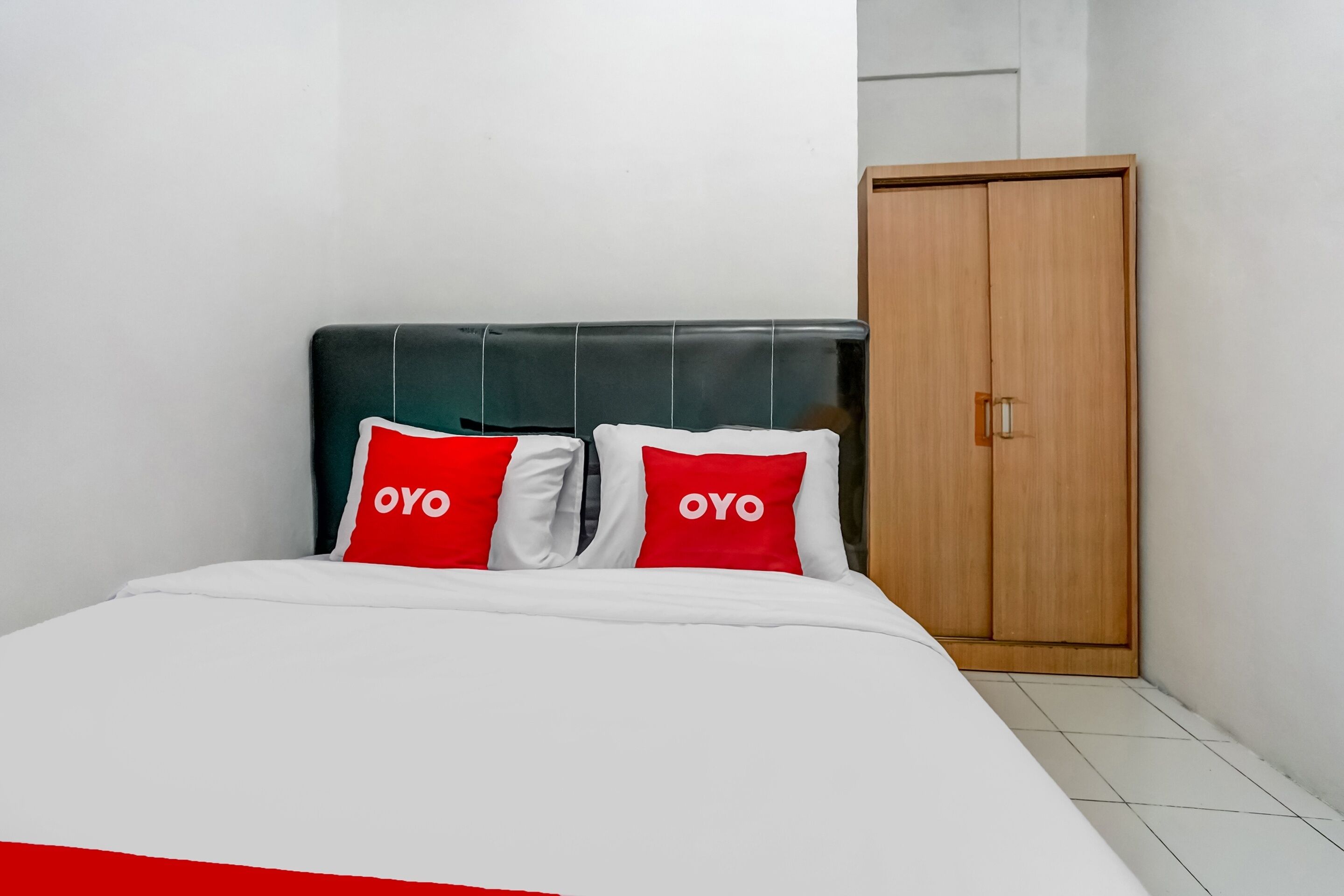 A bed with white bedding and two red pillows with the word "OYO" on them.