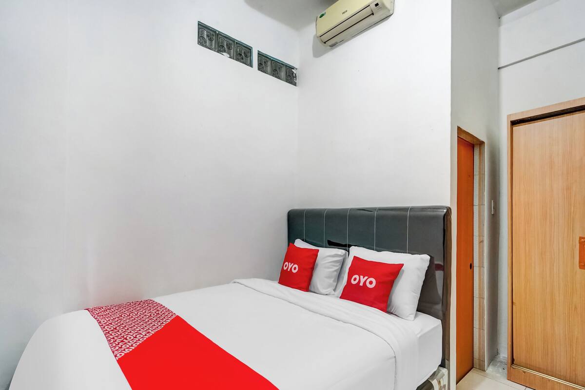 A hotel room with a bed, a wooden door, and an air conditioning unit on the wall.