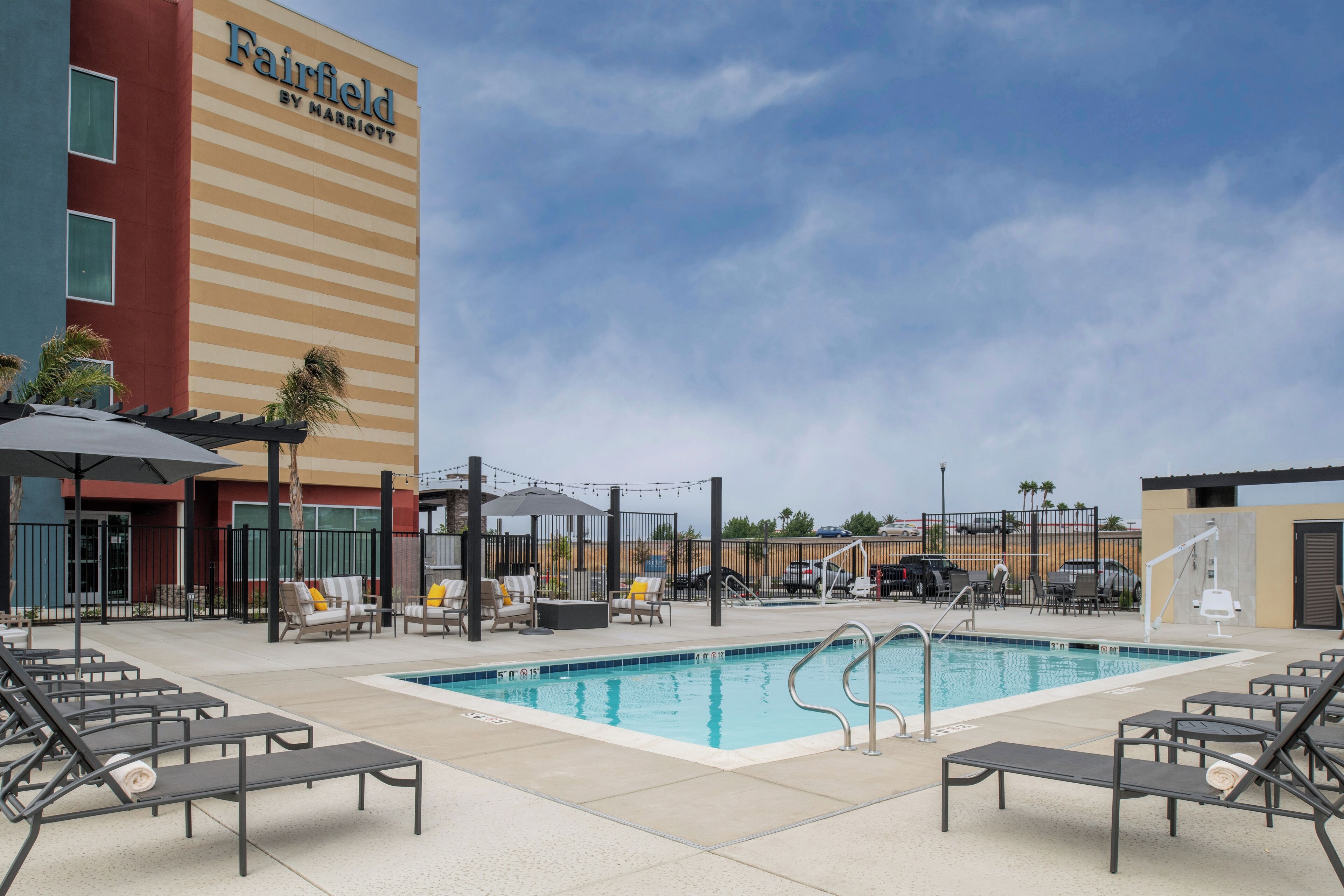 A pool area with lounge chairs, a pool, and a Fairfield by Marriott hotel building in the background.
