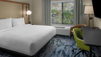 A hotel room with a large bed, a desk, a chair, and a window with a view of trees.