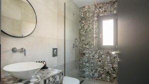 Un bagno con parete doccia in mosaico di pietra, un lavabo bianco e uno specchio.