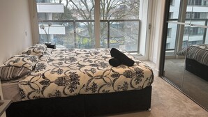 A bedroom with a large window, a bed with patterned bedding, and a view of buildings and trees outside. - Remarkable 2-bedroom Apartment Near Kings Cross (London)