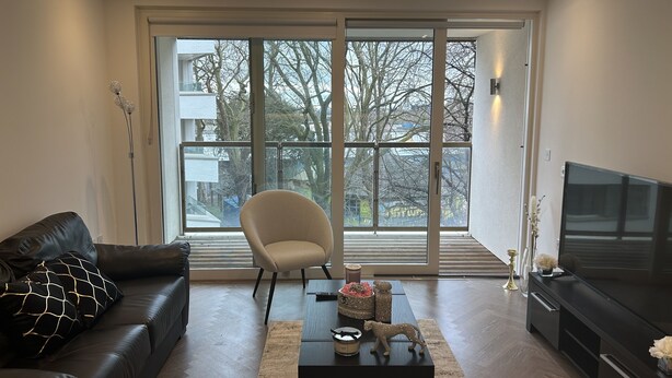 A modern living room with a leather sofa, a white armchair, a coffee table, and a TV. - Remarkable 2-bedroom Apartment Near Kings Cross (London)