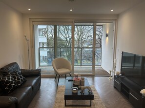 A modern living room with a leather sofa, a white armchair, a coffee table, and a TV. - Remarkable 2-bedroom Apartment Near Kings Cross (London)