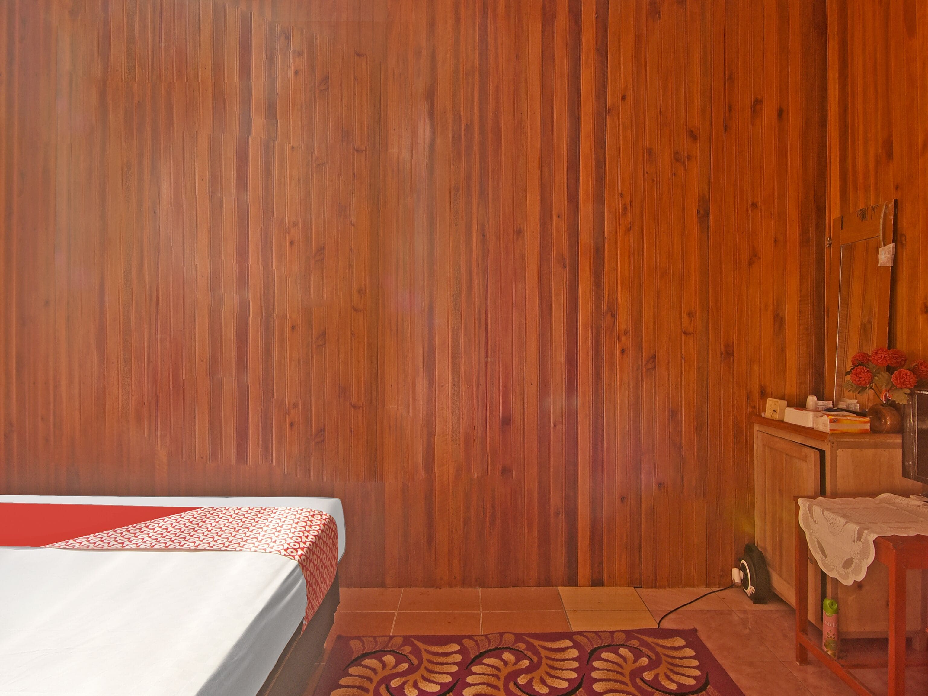 Une pièce avec un lit, un mur en bois, une petite table sur laquelle est posé un vase de fleurs et un miroir.