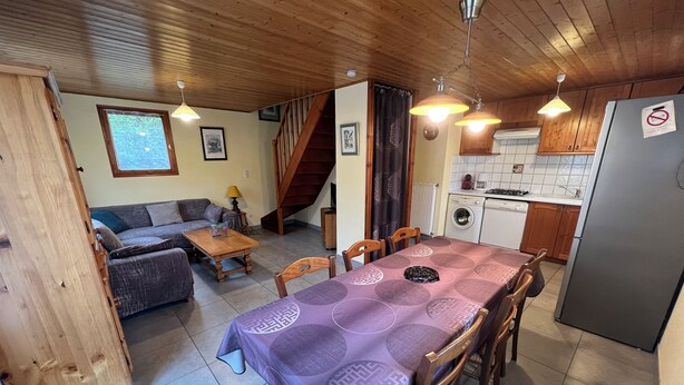 A cozy living area with a sofa, a wooden dining table, and a kitchen with a refrigerator. - 6-person chalet in the heart of Champsaur (ST JEAN ST NICOLAS)