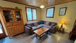 A living room with a wooden ceiling, a sofa, a coffee table, and a cabinet. - 6-person chalet in the heart of Champsaur (ST JEAN ST NICOLAS)