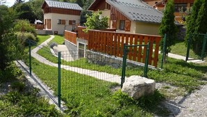 A residential area with wooden houses, a fenced garden, and a gravel path. - 6-person chalet in the heart of Champsaur (ST JEAN ST NICOLAS)