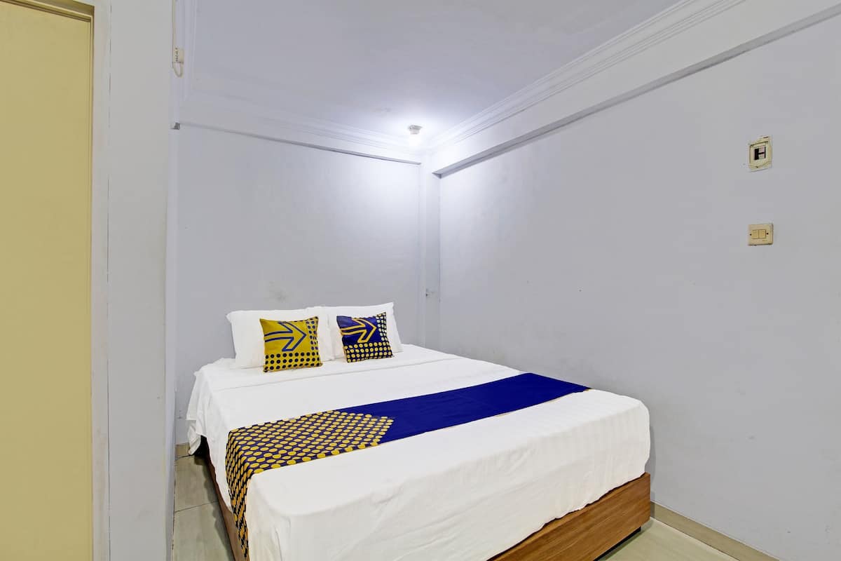 Een kleine, keurig ingerichte slaapkamer met een enkel bed, witte muren en een plafondlamp.