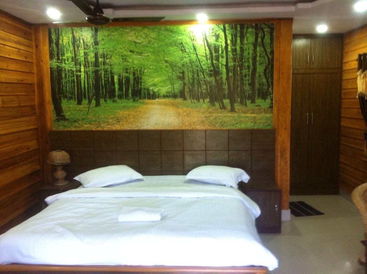 Un dormitorio con una cama grande, paredes de madera, cabecera con un mural de bosque y un armario.