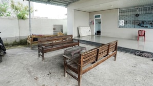 A covered outdoor area with wooden benches, a red chair, and a mattress on the floor.