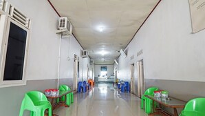 A hallway with green and blue plastic chairs, tables, and air conditioning units on the walls.