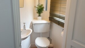 A compact bathroom with a toilet, sink, and a potted plant on the toilet tank. - Charming Studio Sleeps 2 - Kentish Town Nwlondon (London)